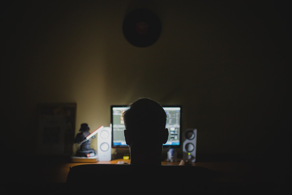 暗い部屋でパソコンを見つめる男性の後頭部